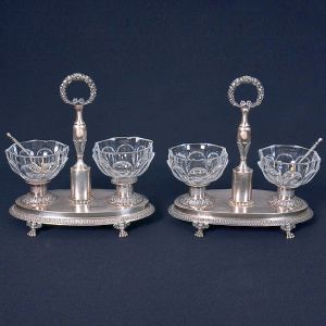 <b>Par de saleiros </b>em prata francesa, com base ovoide sobre quatro pés, corpo cinzelado com motivos fitomórficos e recipientes em cristal lapidado com colheres. Falta um dos pés. Alt. 18 cm