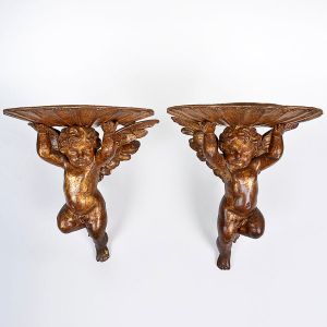 Lindo <b>par de peanhas </b>barrocas representadas por figuras de anjos sustentando apoios em forma de "coquilles". Pátina dourada por toda a extensão do conjunto. Início do séc. XIX. Alt. 30 cm