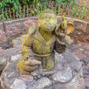 <b>Escultura em pedra </b>entalhada, representando figura ajoelhada, personagem de inspiração franciscana, em atitude contemplativa, ladeada por aves pousadas sobre os ombros e mãos. Alt. 60 cm