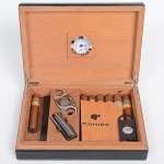 <b>Humidor para charutos </b>em madeira revestida, com interior em cedro e hidrômetro fixado na tampa. Acompanha cortadores metálicos, isqueiro e charutos da marca Cohiba. Med. 28 x 20,5 cm
