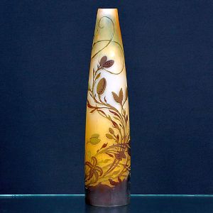 <b> Gallé</b>- Vaso em vidro camafeu, com fundo âmbar e sobreposição em tom castanho, trabalhado em relevo com motivo vegetalista de ramos e folhagens sinuosas. Assinado na base. Alt. 37 cm