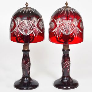 <B>Par de "abatjours" </b>em cristal rubi "overlay" lapidado. Cúpulas em forma de campânula decoradas com entalhes geométricos e motivos em estrela. Bases torneadas no mesmo tom. Alt. 45 cm
