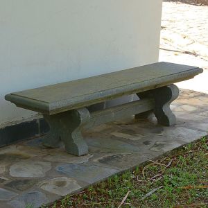 <b>Banco </b>em pedra, com assento retangular liso e bordas boleadas, apoiado sobre dois pés em formato de voluta ligados por travessa central. Apresenta pequenas rachaduras no assento.