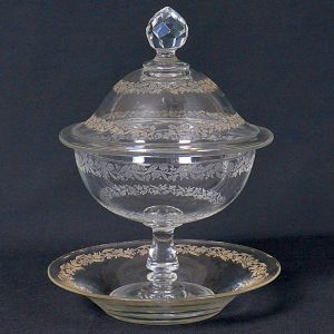 <b>Compoteira e respectivo "presentoir" </b>em cristal lapidado com tampa decorada. Corpo transparente adornado por delicadas gravações florais, apoiado sobre base sólida. Alt. 25 cm