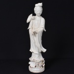 <b>Escultura </b>em porcelana chinesa "blanc de chine" representando "Kwan Yin", a Deusa da Misericórdia, segurando flor de Lótus, símbolo da pureza. Séc. XVIII / XIX. Alt. 46 cm
