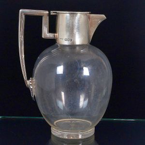 <b>Jarra bojuda </b>em cristal liso com montagem em prata lisa composta de bico, tampa e alça. Contraste da cidade de Londres de 1901 e marca do prateiro JG & S. Alt. 18,3 cm