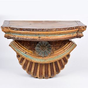 Peanha em madeira entalhada e policromada com parte superior movimentada, roseta ao centro e base com gomos em baixo relevo. Realces a ouro. Séc. XIX. Med. 45 x 58 cm