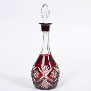 <b>Garrafa </b>em cristal overlay vermelho, lapidada em motivos geométricos e flores estilizadas. Corpo de bojo arredondado e gargalo alongado com tampa facetada. Alt. 31 cm