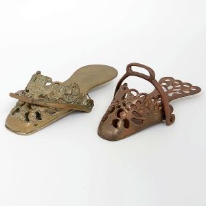 <b>Par de sapatas </b>em bronze fundido, com frente recortada e elaborada decoração vazada de volutas e arabescos em relevo, apresentando leve pátina do tempo. Compr. 20 cm