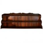 <b>Prateleira </b>em madeira de tonalidade castanha, com três níveis, laterais recortadas em linhas sinuosas e parte superior com recorte decorativo. Med. 64 x 190 cm