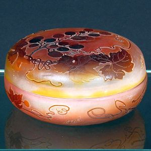 <b>Gallé</b> - Caixa  em vidro camafeu com fundo rosado e sobreposição em tom castanho, decorada em relevo com ramos e cachos de uvas. Assinada na lateral. Diâm. 14 cm