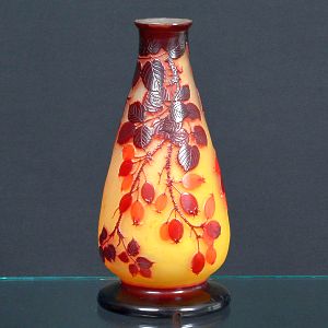 <b>Gallé</b> - Vaso em vidro camafeu com fundo âmbar e sobreposição em tom rubi, decorado em alto-relevo com ramos e frutos estilizados. Assinado na base. Alt. 25 cm