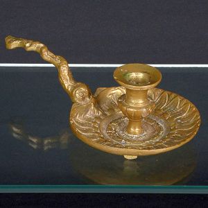 <b>Palmatória </b>em bronze fundido, com pega longa e base circular ornada em relevo com motivos folheados. Apresenta marcas do tempo e pátina de uso. Compr. 20 cm