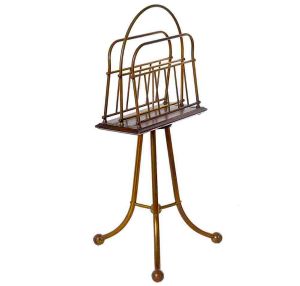 <b>Revisteiro </b>em bronze e madeira. Estrutura em metal dourado com haste central tripla terminada em pés recurvos terminados por esferas. Compr. 74 cm