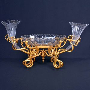 <b>Centro de mesa</b> em cristal lapidado com estrutura em bronze dourado, composto por "bowl" central e duas cornucópias laterais. Med. 44 x 82 cm