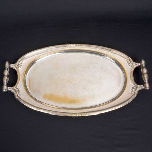 <b>Bandeja </b>oval em metal prateado. Centro liso e bordas decoradas por frisos em relevo e alças trabalhadas em formato da rocalha. Compr. 54 cm
