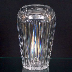 <b>Vaso </b>em cristal lapidado, com corpo cilíndrico, lapidações verticais e faixa superior com recortes geométricos facetados. Alt. 24 cm