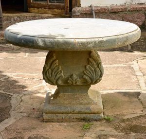 <b>Mesa </b>em pedra lavrada, com tampo circular espesso apoiado sobre base central decorada com folhagens em relevo.