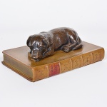 <b>Peso de papel </b>em bronze, representando cão deitado sobre livro. Apresenta pequeno bicado. Compr. 16 cm