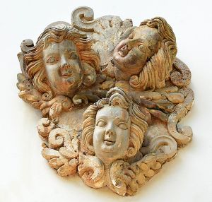 <b>Placa em pedra </b>esculpida, decorada com três cabeças de anjos em relevo, entre volutas e folhagens.