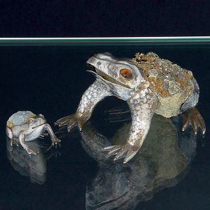 <b>LUIZ FERREIRA </b>- Raro conjunto de duas esculturas de coleção, em forma de rã, em pirita com montagem em prata portuguesa. Trata-se de peça de forte simbologia onde a rã é associada a energia vital e renascimento, transformação, fertilidade e sorte. Peça montada em pirita, sulfeto metálico, conhecido por sua cor amarela dourada e brilhante. Como cristal é associada à prosperidade, riqueza, força e coragem, sendo utilizada para atrair abundância e proteger contra energias negativas. Olhos em olho de tigre. Contrastes da cidade de Porto, 833 ml e punção do referido ourives. Med. da maior 7 x 12 cm