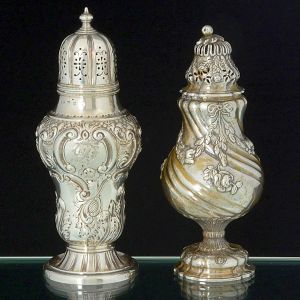 Lote constando de: a) <b>Polvilhador </b>em prata holandesa, piriforme, decorado com guirlandas floridas e laços sobre torcido de gomos. Tampa e base com os mesmos elementos decorativos. Pega em modelado de fruto. Contrastes do séc. XIX. Alt. 20 cm; b) Belo <b>polvilhador </b>em prata inglesa piriforme. Bojo profusamente decorado em composições de flores, folhas e arabescos. Na face anterior reserva monogramada. Pega em modelado de pinha. Contraste da cidade de Birmingham de 1878 e marcado prateiro D & F. Alt. 21,5 cm