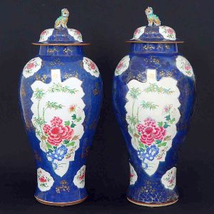 <b>Par de importantes vasos </b>em porcelana Companhia das Índias, decorados em rica policromia Família Rosa com reservas em forma de grandes folhas decoradas com peônias e ramagens de bambus. Outras reservas menores com os mesmos motivos decorativos e restante do bojo em esmalte "powder blue" com arabescos realçados a ouro. Pegas das tampas modeladas em cães de fó em esmaltes verdes, azuis e amarelos. Reinado Qianlong. Séc. XVIII. Um deles com restauro na parte superior. Alt. 74 cm