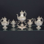 <b>Serviço de chá e café </b>de grandes dimensões em prata portuguesa. Decoração em elementos fitomórficos e "coquilles" em composições no estilo D. João V. Alças dos bules encimada por cornucópias de flores e pássaros terminadas em cabeças de patos. Contraste da cidade do Porto do séc. XIX. Constando de bule para água quente e sua trempe, bule para café, bule para chá, leiteira e açucareiro (alça e tampa do bule de chá necessita solda). Alt. do samovar 39 cm. Peso 5805 gramas.