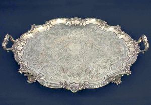 <b>Bandeja </b>de forma oval em prata inglesa do período William IV. Fundo centralizado por brasão armorial e lavrado com volutas, "coquilles" e texturizados. Borda movimentada decorada por godrões intercalados por "coquilles". Alças recamadas por folhagens e pés acompanhando os mesmos motivos descritos. Contraste da cidade de Londres de 1834 e marca do prateiro da casa real britânica ROBERT GARRARD. No verso inscrição Garrard  Panton Street  London. Med. 70,5 x 51 cm