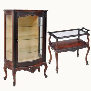 <b>Lote</b> constando de: a) Vitrine "bombée" em jacarandá escurecido apresentando frente e laterais envidraçadas, saia baixa com florão ao centro e pernas recurvadas. Interior forrado em veludo na cor pêssego. Selo da loja Bertalan Móveis Ltda. Med. 151 x 90 x 38,5 cm; b) Carrinho de chá em jacarandá construído em dois "plateaux", sendo o superior em vidro com duas alças laterais. Pernas recurvadas terminadas em rodinhas. Séc. XIX. Med. 77 x 43 x 82 cm