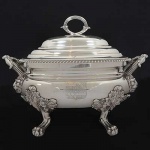 <b>Sopeira </b>oval em prata inglesa do período George III. Brasão armorial na face anterior e timbre na tampa. Borda em godrões. Alças frisadas recamadas por estilizações vegetais, elementos concheados e implantadas em cabeças de leões. Pés em garras encimadas por volutas. Pega da tampa acompanha o estilo. Contraste da cidade de Londres de 1816 e marca do prateiro WILLIAM BATEMAN. Peso 4185 gramas. Med. 31 x 41 x 26 cm