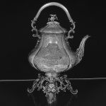 Belíssimo <b>chaleiro e trempe </b>em prata inglesa vitoriana, apresentando parte inferior bojuda e decoração em gomos lavrados de motivos vegetais. Ao centro escudo armorial. Tampa encimada por arranjo de flores e isoladores em marfim. Contraste da cidade de Londres de 1852 e marca do prateiro CHARLES REILY & GEORGE STORER. Recipiente da trempe com marca do período George IV de 1825. Alt. 42 cm. Peso 2490 gramas.