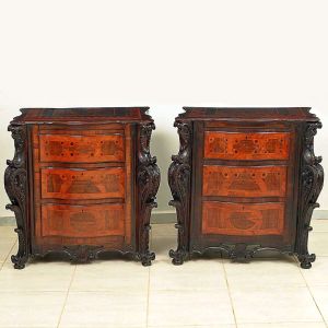 Belíssimo <b>par de cômodas </b>portuguesas construídas em madeiras raras. Apresentam forma retangular movimentada e robustas colunas escurecidas, vigorosamente esculpidas com volutas e folhas de acanto. Três gavetas anteriores, florão na parte inferior e pés enrolados. Apresenta belo trabalho em "marqueterie" ornamentado com frisos e estilizações geométricas. Séc. XVIII / XIX. Med. 86,5 x 92 x 54 cm