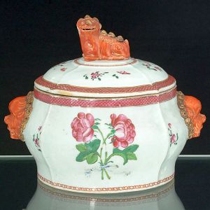 Belíssima <B>sopeira </B>circular em porcelana Companhia das Índias apresentando bojo de forma "bombée" e decoração em policromia florida nos esmaltes da Família Rosa. Pegas do bojo modeladas em cabeças de cães de fó em "rouge de fer" realçados a ouro e tampa no referido animal em posição sentada. Séc. XVIIIU. Interior com selo do famosa antiquário Vetmas de Buenos Aires. Compr. sem as alças 25 cm; Alt.19 cm