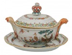 <B>Sopeira miniatura com seu "presentoir" </B>em porcelana Companhia das Índias decorada em policromia nos esmaltes da Família Rosa com figuras e aves entre paisagem com edificações. Restante das peças com guirlandas floridas. Pegas do bojo modeladas em carrancas emplumadas e da tampa em coroa vazada. Séc. XVIII. "Presentoir" com restauro. Compr. do "presentoir" 18,5 cm; Compr. da sopeira 18 cm