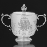 <b>"Porringer" com sua tampa </b>em prata inglesa decorada com lavrados fitomórficos e ondulações. Ambas as faces com reservas, uma monogramada e outra datada, envolvidas em ramagens com cachos de uva. Pega da tampa modelada em pinha e alça com carrancas antropomorfas. Contraste da cidade de Londres de 1906 e marca do prateiro S & Cº. Compr. 25 cm; Alt. 19,5 cm. Peso 800 gramas.