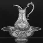 <B>Jarro e bacia </B>em prata portuguesa decorada em elegantes composições floridas com volutas e angras. Alça recurvada implantada em máscara antropomorfa. Bacia com os mesmos motivos decorativos. Apresenta reserva monogramada. Contraste "Javali" da cidade do Porto, 833 ml, usado de 1886 a 1938. Bocal com amassado. Alt. do jarro 44 cm; Diâm. da bacia 49,5 cm. Peso 4665 gramas.