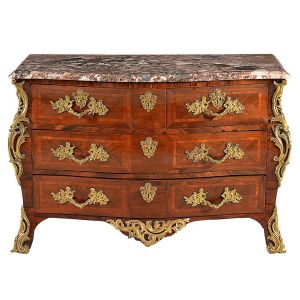 Belíssima <b>cômoda </b>francesa Régence construída em madeiras nobres europeias. Caixa retangular em movimento "bombée", apresentando duas gavetas lado a lado sobre dois gavetões. Tampo em mármore rajado. Lindas e elaboradas ferragens em bronze ormolu decoradas com cupidos e composições com máscaras antropomorfas. Ilhargas e pés em volutas. Séc. XVIII. Med. 87 x 127 x 65 cm