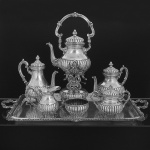 Elegante <b>serviço para chá e café </b>em prata Sterling 925 ml peruana. Todas as peças decoradas com gomos e alças recamadas por volutas. Pernas recurvadas e isoladores em marfim. Constando de bandeja (compr. 76 cm), chaleira e sua trempe (alt. sem a alça 41 cm), bules para café e chá, leiteira, açucareiro e "bowl" para pingos. Marca do prateiro CAMUSSO. Peso 6840 gramas.