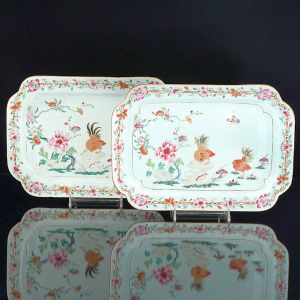 <b>Par de travessas</b>  retangulares de cantos chanfrados em porcelana Companhia das Índias pertencente ao "Serviço dos Galos", de D. João VI. Decoração em policromia nos esmaltes da Família Rosa representando vista de jardim com rochedos, flores e dois galos. Período Qianlong. Séc. XVIII. Serviço trazido pelo monarca por conta de sua mudança para o Brasil. Compr. 31,5 cm