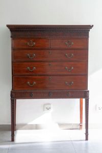 Belo <B>móvel inglês Chippendale</B>, em mogno, conhecido como "chest on stand". Apresenta duas gavetas sobre três gavetões e pernas retas terminadas em ponteiras. Entalhes rasos em geometrizados nas superfícies superior e inferior. As pernas são decoradas por goivos superpostos encimados por rosetas. Ferragens da época. Séc. XIX. Med. 164 x 117 x 57 cm