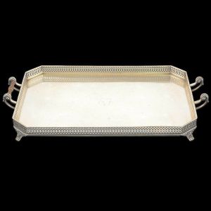 <b>Bandeja</b>  em prata portuguesa retangular de cantos chanfrados. Apresenta fundo liso monogramado, galeria vazada em composições circulares e pés em garras. Duplas alças em segmentos torneados implantados em volutas. Contraste a cidade de Lisboa usado a partir de 1938 e marca de prateiro. Falta uma pega de madeira. Compr. 58 cm. Peso 2615 gramas.