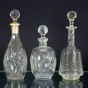 <b>Conjunto de 3 garrafas </b>em cristal transparente com lapidações distintas. Uma de corpo alongado, apresentando bojo decorado com lapidação em formato estrelado e gargalo com acabamento em metal, outra mais abaulada, com lapidação profunda de motivos geométricos e florais, e a terceira, de corpo cilíndrico afilado e lapidação vertical em gomos.