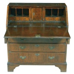 <b>Cômoda escrivaninha </b>inglesa construída em raiz de nogueira. Apresenta quatro gavetinhas sob seis escaninhos centralizando cofre central. Dois compartimentos secretos com face anterior entalhada em colunas. Tampo rebatível. Parte inferior composta de três gavetas superpostas. Ferragens de época. Séc. XVIII. Med. fechada 101,5 x 91 x 51 cm