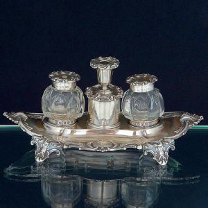 <b>Tinteiro </b>oval em prata inglesa vitoriana decorada com volutas e acantos e duas reservas no centro de ambos os lados. Laterais com dois vidros em cristal lapidado em arcos ogivais e ao centro pequeno castiçal sobreposto a compartimento cilíndrico. Contraste da cidade de Sheffield de 1850 e marca do prateiro Hy Wilkinson & Co. Compr. 24 cm