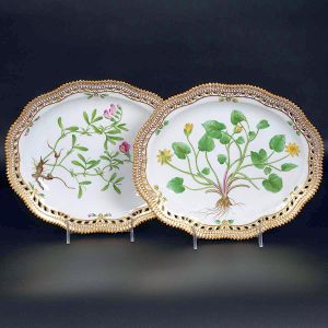 <b>Par de travessas </b>ovais com bordas reticuladas em porcelana dinamarquesa da importante manufatura Royal Copenhagen modelo "Flora Danica". Cada peça, inteiramente pintada à mão em belíssima policromia com suas designações botânicas e numeração no verso. Apresenta borda em mínimos picotados cobertos a folha de ouro. Med. 27 x 22,5 cm