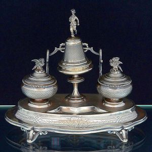 <b>Tinteiro </b>em prata francesa do séc. XIX. Bandeja com trabalhos guilhochados. Recipiente para escrita encimado por aves e sineta ao centro com pega em figura de oficial (necessita solda). Parte posterior com suporte para pena monogramado ao centro. Contraste "Cabeça de Mercúrio" usado de 1840 a 1879. Compr. 29,5 cm. Peso 490 gramas.