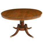 Bela <b>mesa circular </b>inglesa, período "Regency" construída em jacarandá "kingwood". Apresenta tampo decorado com embutidos metálicos em segmentos de motivos vegetais. Haste central em segmentos torneados sobre "plateau" circular e com pernas recurvas terminadas em garras metálicas. Início do séc. XIX. Alt. 67 cm; Diâm. 121,5 cm