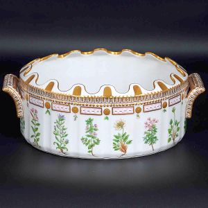 Excepcional "<b>rafraîchissoir</b>" oval de borda ondulada em porcelana dinamarquesa da importante manufatura Royal Copenhagen modelo "Flora Danica". Inteiramente pintada à mão em belíssima policromia com suas designações botânicas e numeração no verso. Apresenta borda em mínimos picotados cobertos a folha de ouro. Med. 33 x 23 cm
