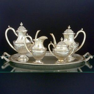 <b>Serviço para chá e café </b>em prata portuguesa decorada em gomos, alças recurvadas e pegas modeladas em pinhas. Isoladores em marfim. Contraste da cidade de Lisboa usado a partir de 1938. Constando de bandeja, bules para chá e café, leiteira e açucareiro. Compr. da bandeja 66 cm; Alt. do bule de café 27 cm. Peso 5400 gramas.